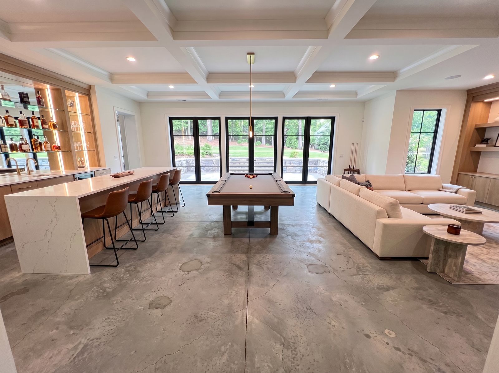 A basement lounge with a bar and a pool table on its old, stained concrete floor, before coating